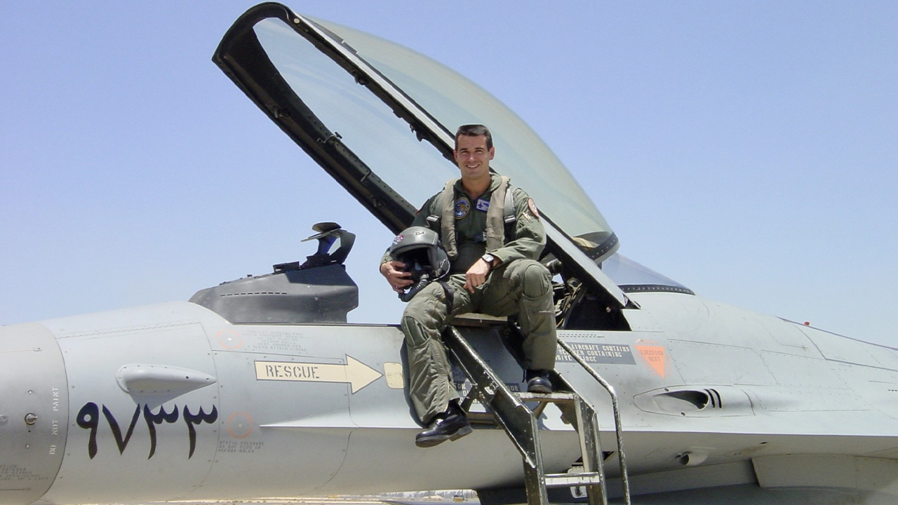 David Bottomlee sits on the wing of a fighter jet parked on a runway