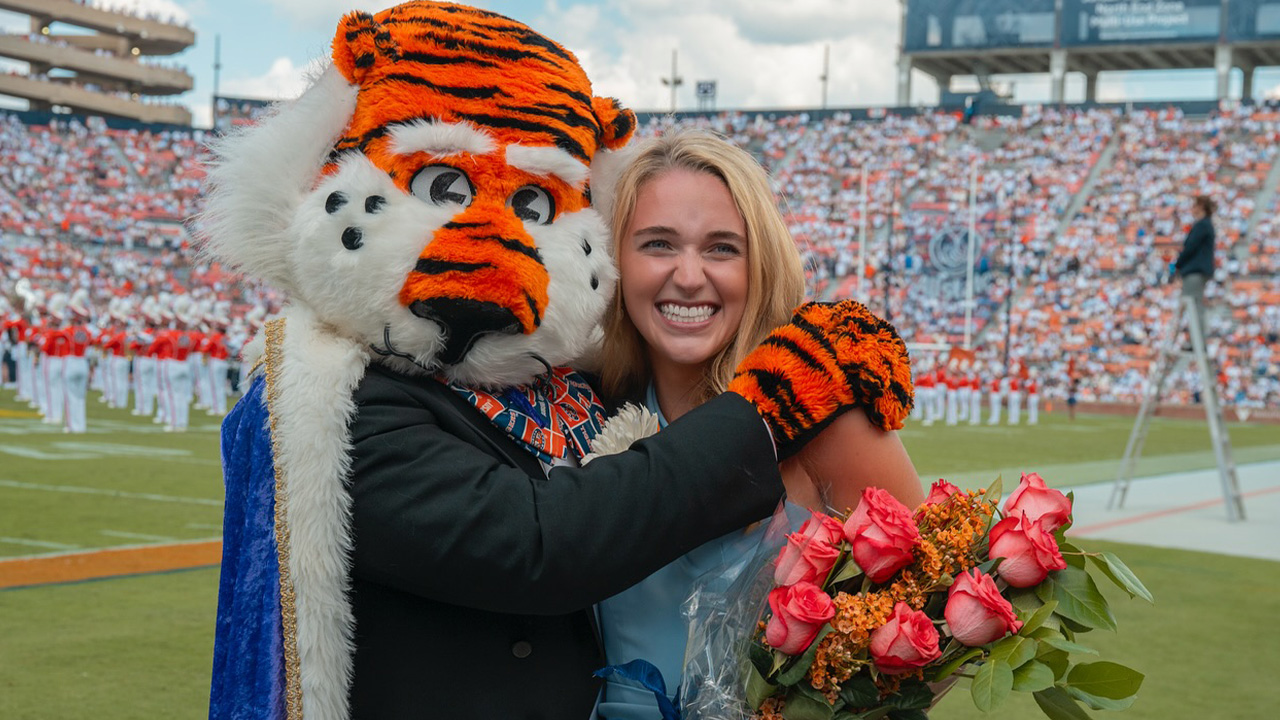 A young woman holding roses hugs Aubie the Tiger