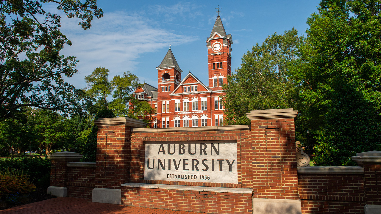 Samford Hall sits in the background behind a brick sign that says Auburn University