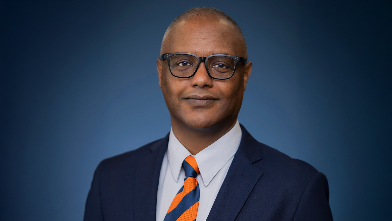Ash Abebe poses for a headshot wearing an orange and blue tie and suit jacket