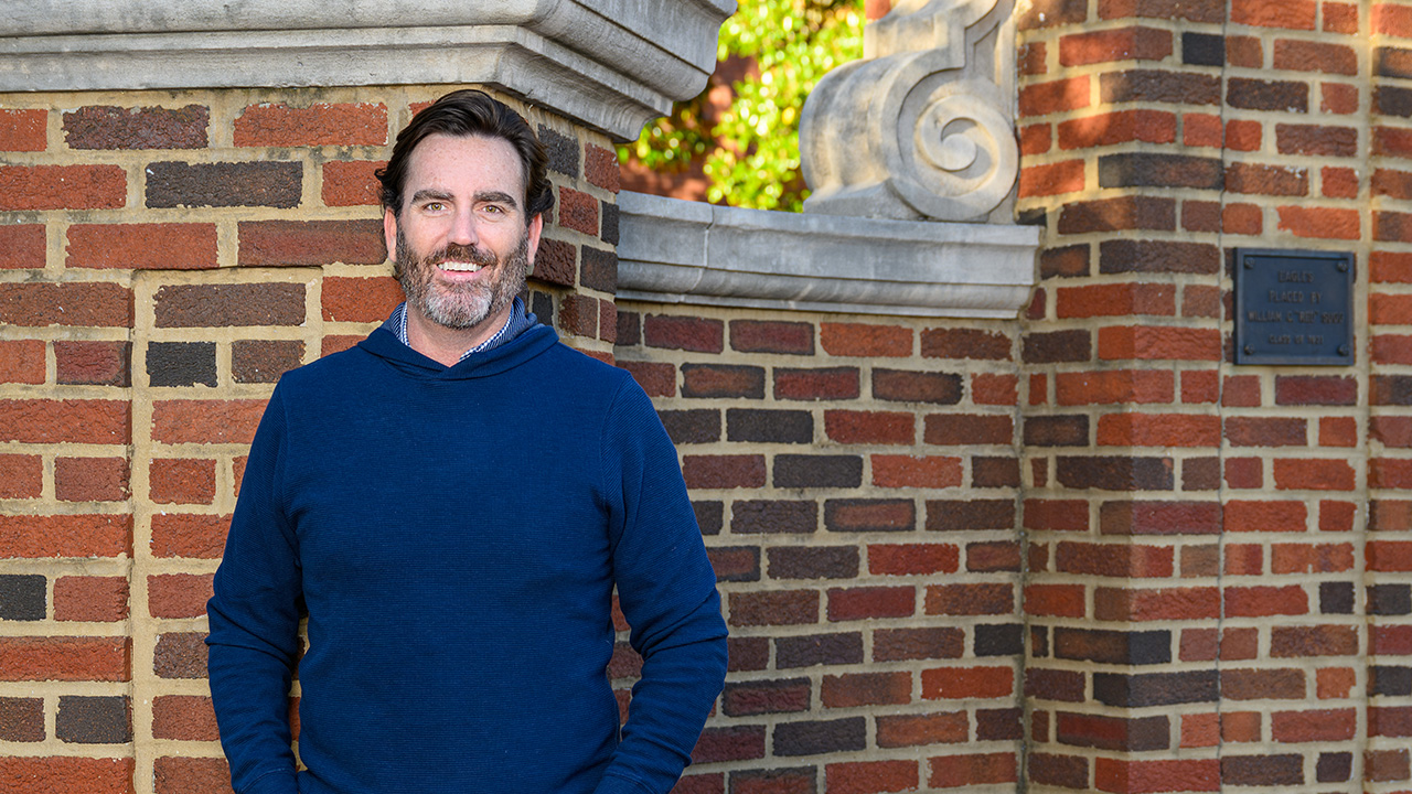 Scott leans against a brick wall on the Auburn campus