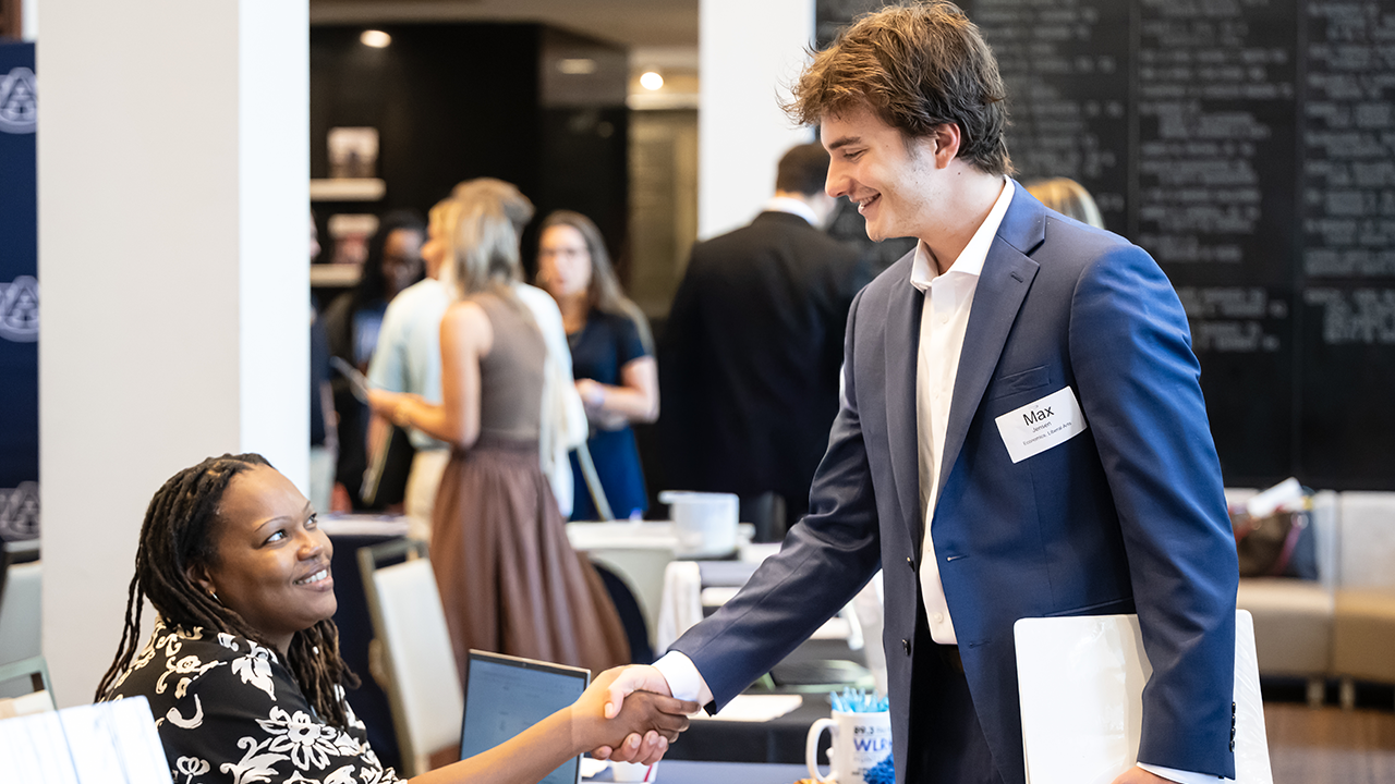 A student shakes hands with a potential employer at a career fair.