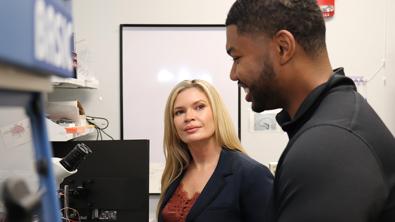 Faculty member and student stand at microscope