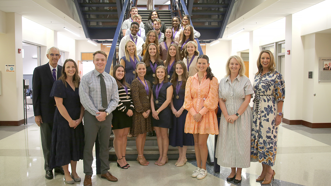 Group of 16 students and faculty members stand on a staricase