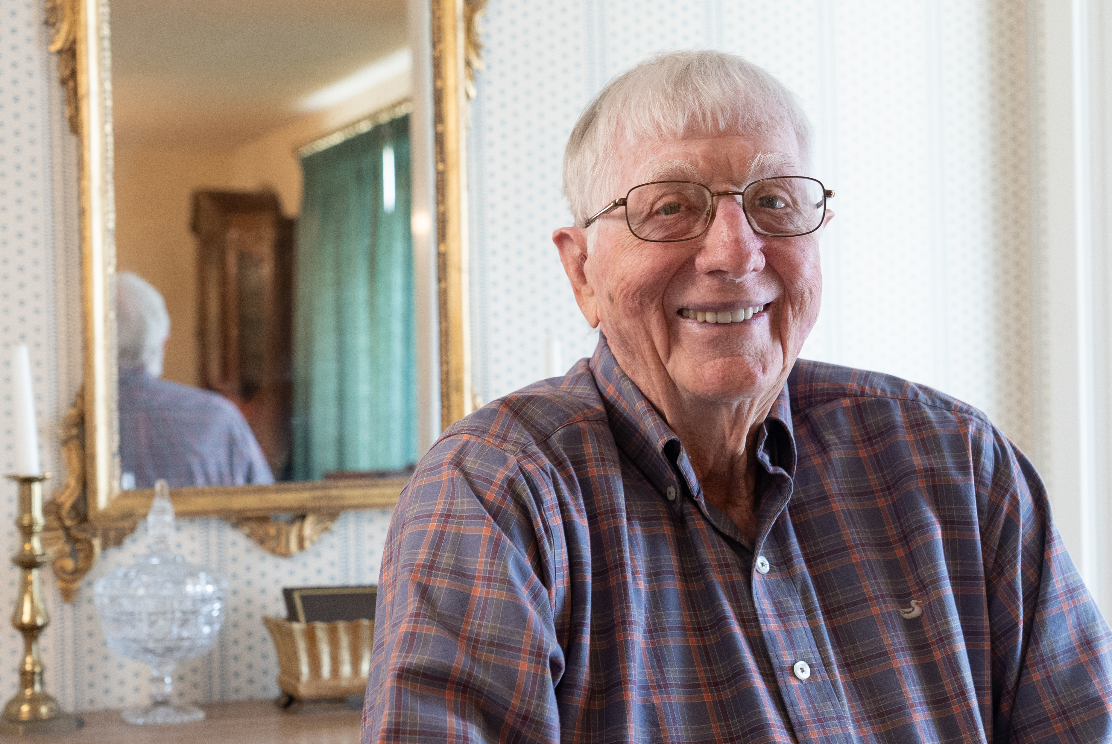 Older man with glasses sitting in front of a mirror. 