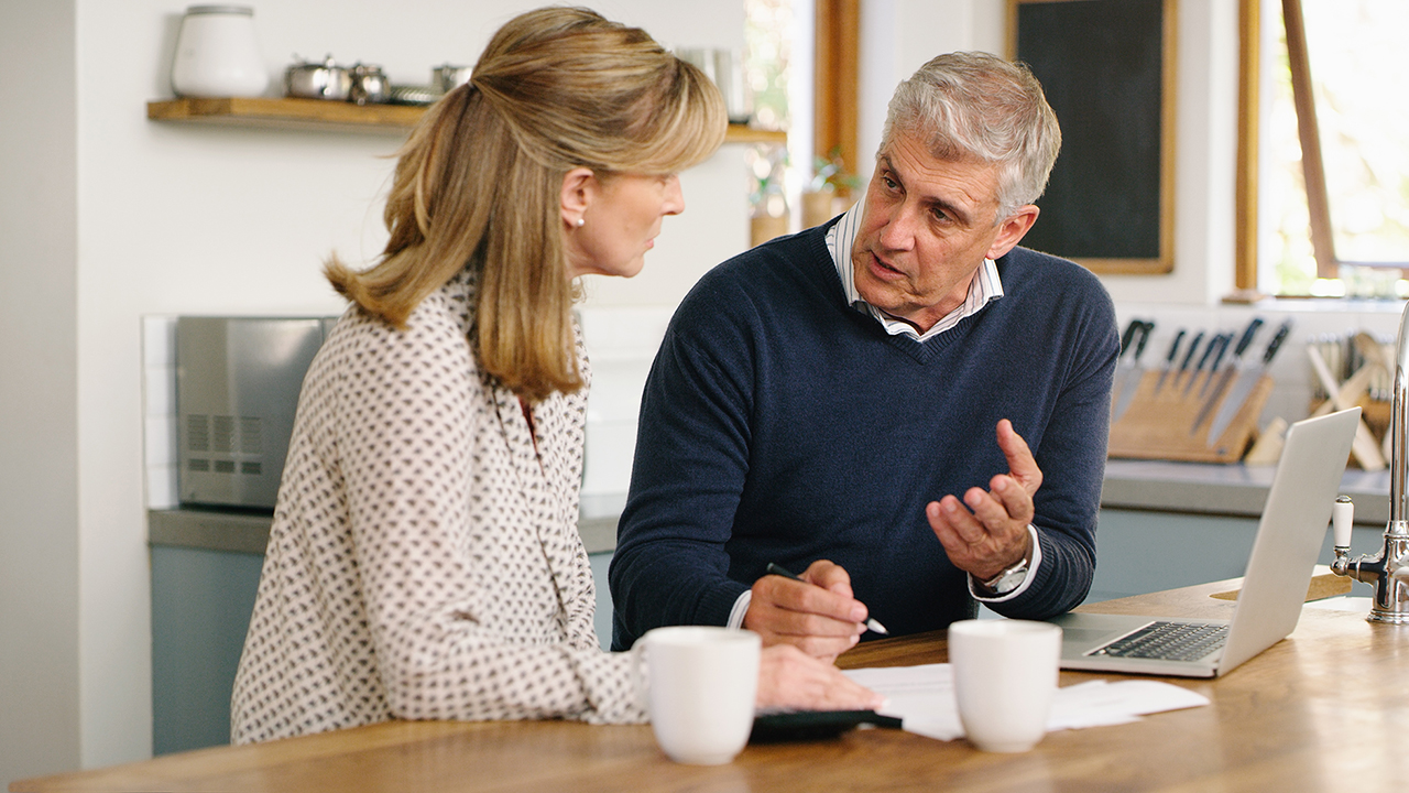 A man and a woman have a discussion at their kitchen table.