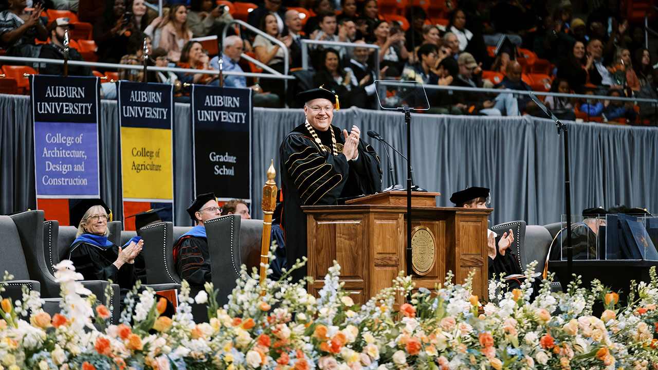 President Christopher B. Roberts stands on stage clapping at a commencement ceremony.
