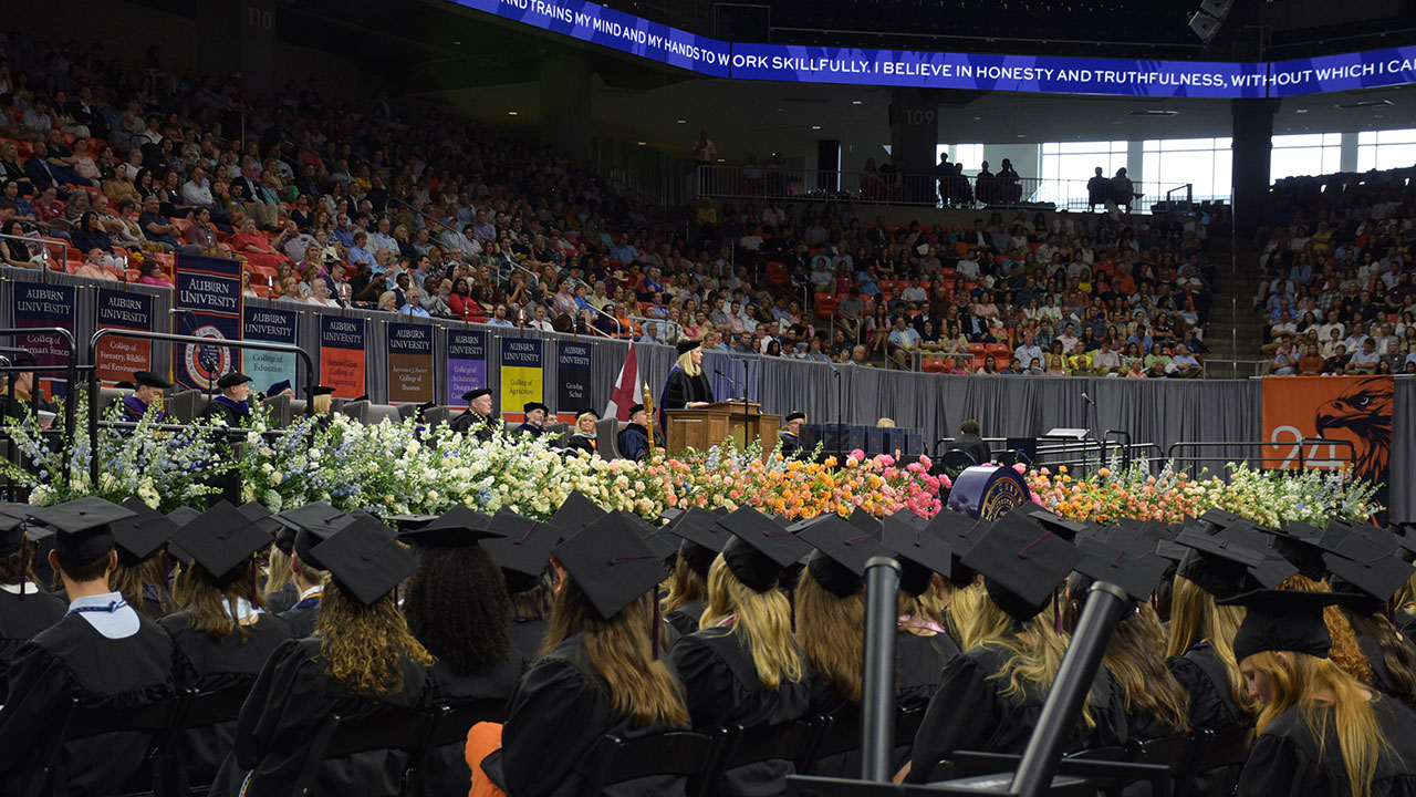 A stage filled with flowers in front of a group of Auburn graduates sitting.