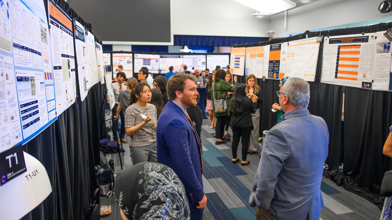 Students and faculty stand and discuss presentations.